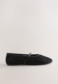 Chaussure plate Mary Jane noire recouverte de petits sequins noirs avec une fine bride et une boucle sur un fond clair.
