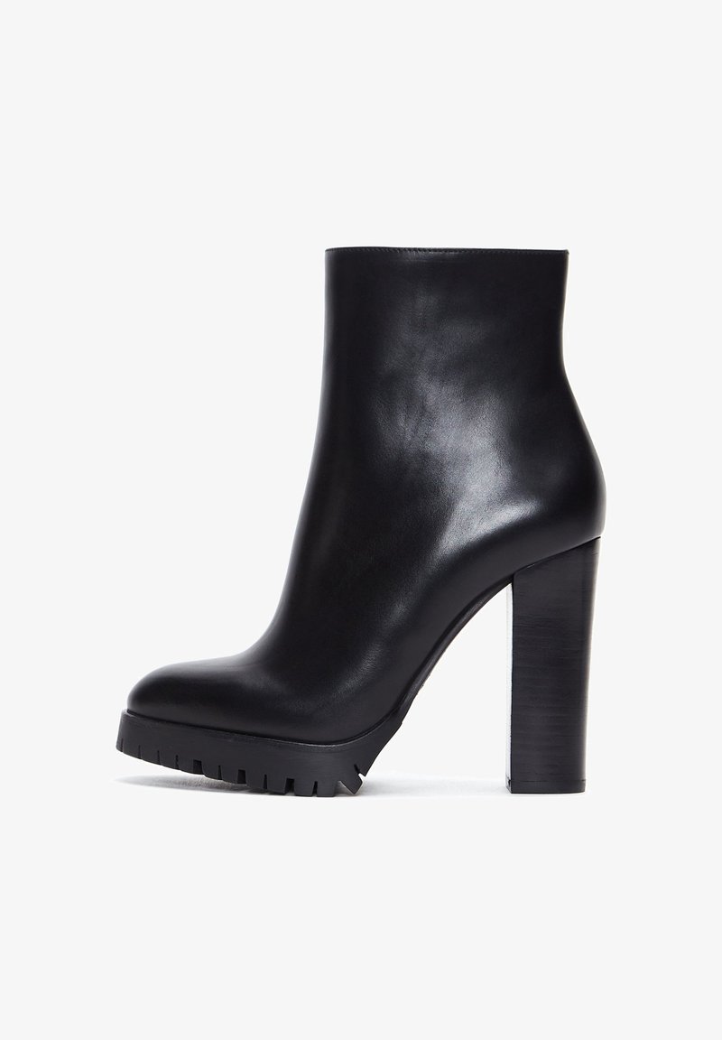 Botte de cheville en cuir noir avec un haut talon bloc et un bout profilé. Semelle épaisse avec un relief robuste. Texture lisse et brillante.