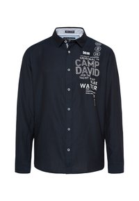Camisa de botones azul marino de manga larga, con bordados y parches en blanco, con un cuello clásico y una textura suave.