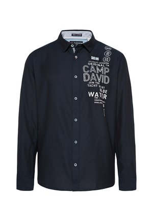 Camisa de botones azul marino de manga larga, con bordados y parches en blanco, con un cuello clásico y una textura suave.