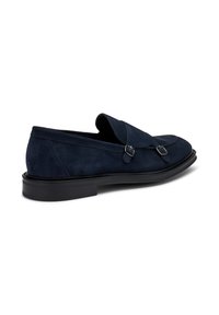 Mocassini in suede blu navy con suola bassa in gomma nera, dotati di due cinturini decorativi con fibbie in metallo e una punta arrotondata.
