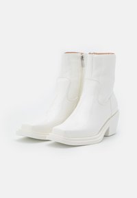 Botas de tobillo de charol blanco con punta cuadrada, cremalleras laterales y tacón grueso. Textura suave con diseño minimalista.