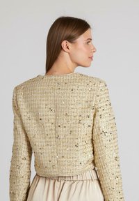 Kurzer, mit Gold-Pailletten besetzter Blazer mit texturiertem Finish, Rundhalsausschnitt und langen Ärmeln, mit schlichter Rückseite und weicher Fütterung.