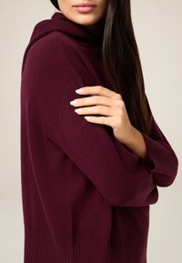 Bordowy sweter z dzianiny z kapturem, wyposażony w prążkowane mankiety i dół. Gładka tekstura i luźny krój. Subtelne detale przeszyć.