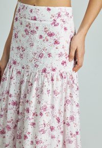 Gonna floreale bianca con fiori rosa e viola, dettaglio a disegno pastorale e design a strati. Realizzata in tessuto leggero con vita aderente.