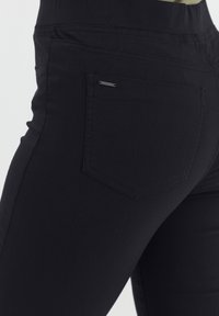 Vaqueros negros con una tela suave y elástica, diseño de cinco bolsillos y una marca sutil en el bolsillo trasero.