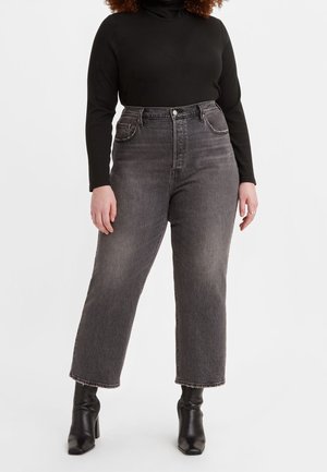 Osoba o krągłych kształtach nosząca czarny długi rękaw, wyblakłe szare jeansy z wysokim stanem z surowymi brzegami oraz czarne skórzane botki na obcasie, stojąca na białym tle.