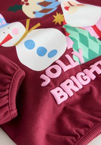 Bordeaux sweatshirt med farverige snemænd og julet grafik. Teksten siger "JOLLY BRIGHT" i pink, med ribbede manchetter og blød tekstur.