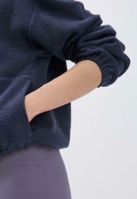 Dunkelblaues Fleece-Sweatshirt mit lässiger Passform, elastischen Bündchen und einer Fronttasche. Trägt man mit grauen Leggings, die die Weichheit des Materials betonen.