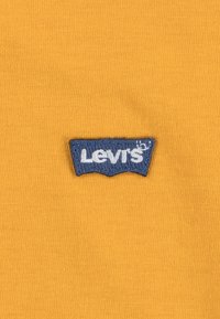 Tessuto giallo con una superficie testurizzata, caratterizzato da un patch con il logo blu di Levi's ricamato al centro.
