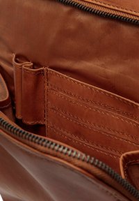 El interior de la bolsa de cuero marrón cuenta con un forro suave, compartimentos para tarjetas y portapapeles. Detalle de cremallera en el borde superior.