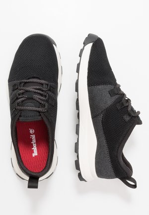 Zapatillas deportivas negras con parte superior de malla y material sintético, entresuela blanca, suela exterior negra gruesa y detalle de marca interior en rojo. Diseño con cordones.