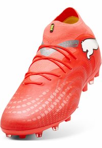 Punainen jalkapallokengän kenkä, jossa on teksturoitu neulottu päällinen, heijastavat yksityiskohdat ja erottuva logo. Sisältää nauhakiinnityksen ja läpinäkyvät nastat.