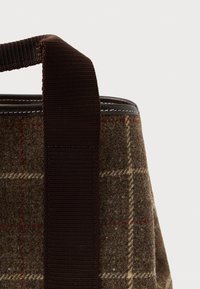 Taška z vlněné směsi s hnědým kostkovaným vzorem, tmavě hnědými tkanými držadly a kontrastním šitím podél okrajů. Kompaktní, strukturovaný design.