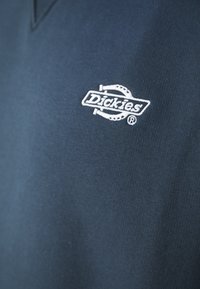 Polo shirt in cotone blu navy con finitura testurizzata, caratterizzato da un logo Dickies ricamato in bianco sul lato sinistro del petto.
