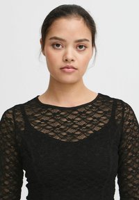 Top nero a maniche lunghe in tessuto di pizzo, caratterizzato da un design a motivo e un collo rotondo con una leggera lucentezza e una silhouette aderente.