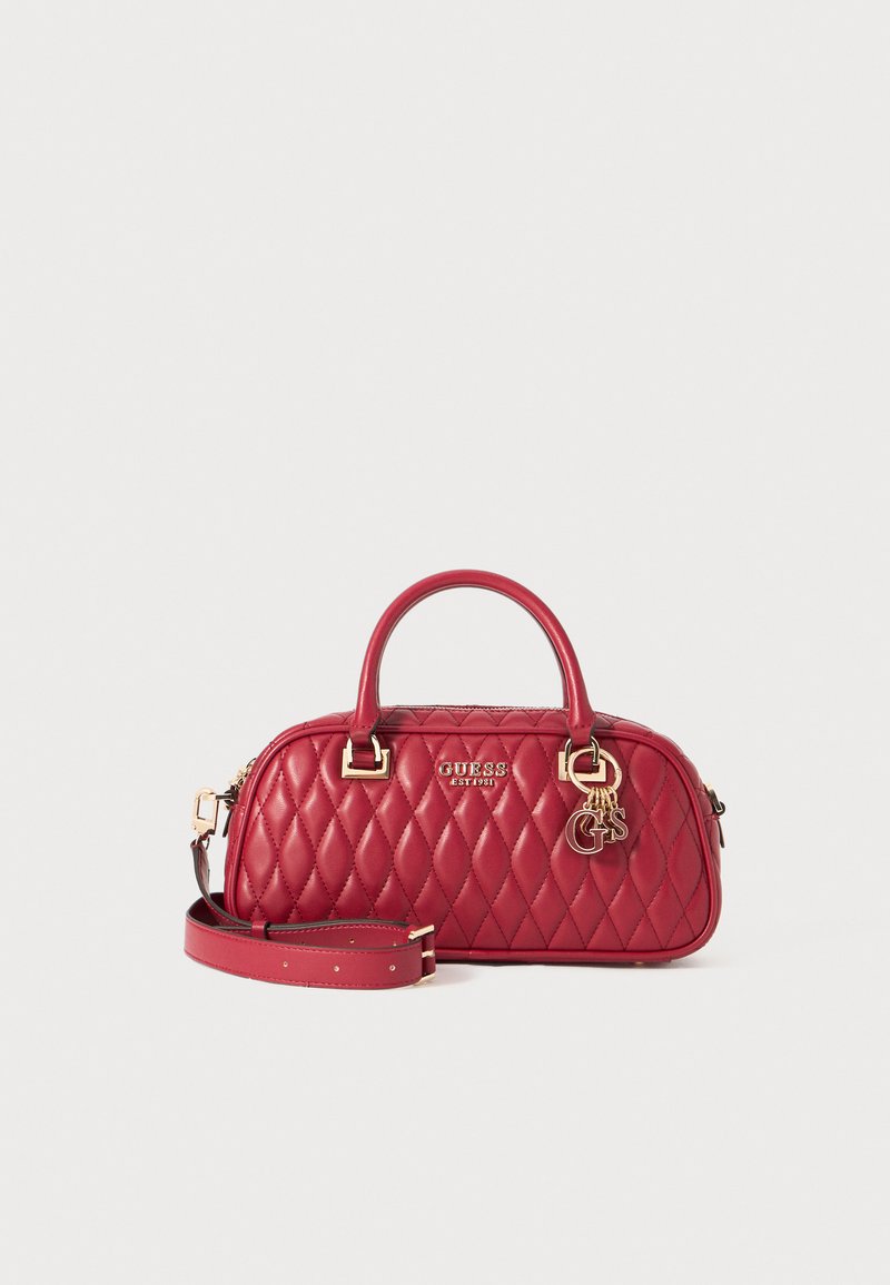 Gequilted rode handtas van synthetisch materiaal met dubbele handvatten, gouden hardware en een afneembare schouderband. Bevat een logo en decoratieve charms.