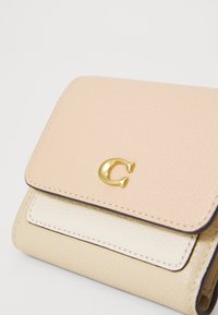 Leather wallet with a light pink and cream color scheme, featuring a textured finish, a metallic gold logo, and contrasting stitching.