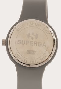 Reloj con correa de silicona gris y fondo de acero inoxidable. La grabación en el fondo incluye "RESISTENTE AL AGUA 3 ATM" y "SUPERGA". Diseño de esfera redonda.