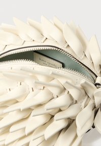 Mala de couro branco com detalhes texturizados em forma de pétala, fecho de correr e interior azul claro. Etiqueta interna com a inscrição "kate spade".