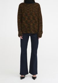 Maglione oversize lavorato a maglia in tonalità scure con macchie gialle, rosse e verdi. Abbinato a jeans svasati scuri e décolleté nere a punta.