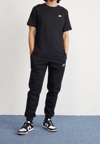 Svart bomull t-shirt med en liten vit Nike-logga; tillsammans med svarta sweatpants och svarta och vita sportskor med snörning.