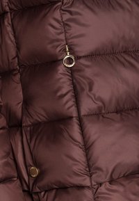 Steppjacke aus dunkelbraunem Nylon mit gesteppten Abschnitten, versehen mit einem goldfarbenen, runden Reißverschlussanhänger und einem runden metallischen Logoknopf.