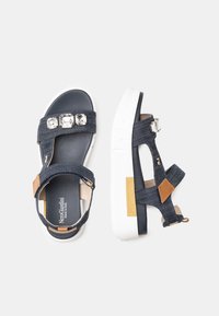 Sandali platform in denim con tre strass trasparenti, dettagli in pelle marrone, cinturini regolabili e una suola bianca spessa.