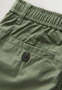 Pantalon vert en tissu avec taille élastique, passants pour ceinture et une poche arrière sécurisée par un bouton foncé.