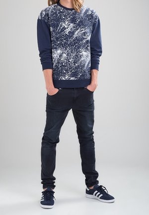 Mörkblå sweatshirt med vit stänkdesign, ihop med mörka jeans och mörkblå sneakers med vita ränder. Avslappnad passform och modern stil.