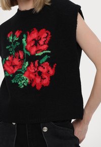 Czarny dziany sweter bez rękawów, z żywym, czerwono-zielonym haftem kwiatowym z przodu, obramowany teksturowanym wykończeniem.