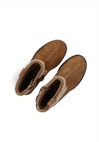 Bruine suède enkellaarsjes met nep bontvoering, ritssluiting en decoratieve witte stiksels die een strikdesign op de bovenkant vormen.