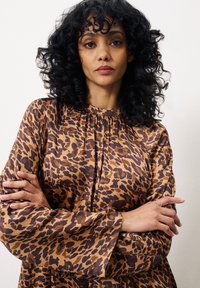Braunes Leopardenmuster-Oberteil mit langen Ärmeln, lässiger Passform und gerafftem Ausschnitt; weicher Stoff mit glatter Textur.
