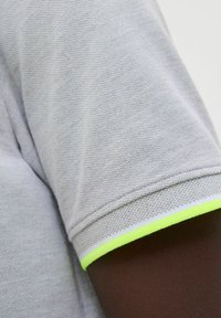 Grau strukturiertes Polohemd mit einem neonfarbenen gelben Akzent am Bündchen, versehen mit weißen und grauen Nähdetails.