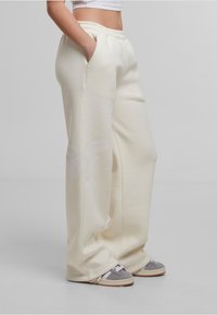 Pantalons de sport crème avec une coupe décontractée, taille élastique, poches latérales et un motif floral subtil sur la jambe gauche.