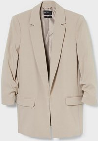 Blazer beige cintré en tissu lisse, doté d'un col cranté, de deux poches avant et de manches légèrement froncées.