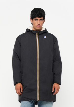 Zwarte lange jas met capuchon, voorzien van een gele en witte ritssluiting en een logo op de borst. Vlies gevoerd interieur voor warmte.