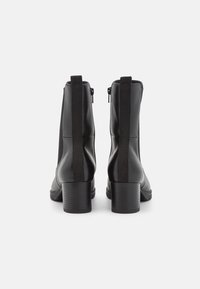 Par de botas de tobillo de cuero negro con tacones cuadrados, tiradores traseros y cremalleras laterales, mostradas desde la parte trasera sobre un fondo blanco.