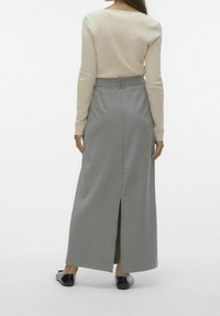 Lång grå kjol med slits bak, hög midja och bältesöglor, i kombination med en figurnära beige långärmad topp. Platta svarta skor synliga.