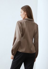 Brown satin blouse with a collared neckline, long balloon sleeves, and a smooth texture, paired with black pants.