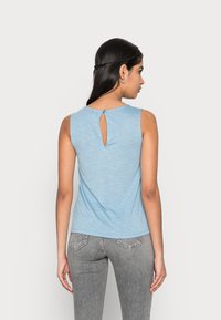 Top sem mangas azul claro com detalhe em recorte nas costas, feito de um tecido suave e texturizado, combinado com jeans ajustados cinza.