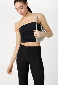 Top noir sans bretelles en tissu extensible avec une texture froncée, associé à un pantalon noir à taille haute et à côtes. Le mannequin tient un sac métallique argenté.