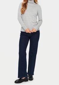 Grauer Rollkragenpullover kombiniert mit dunkelblauen Schlagjeans. Der Pullover hat gerippte Bündchen und eine glatte Textur, während die Jeans eine klassische Passform haben.