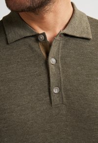 Polo shirt in verde oliva a maglia con colletto, dotato di tre bottoni e un delicato tessuto testurizzato.