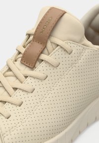 Μπεζ αθλητικό παπούτσι από διάτρητο δέρμα με ταμπά δερμάτινη λεπτομέρεια. Διαθέτει επίπεδα κορδόνια και υφή στην σόλα για καλύτερη πρόσφυση.