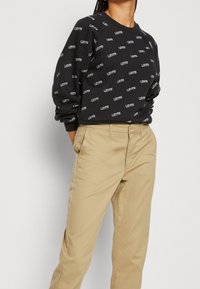 Sweatshirt noir avec impression du logo "LEVI'S" en blanc. Il présente un col rond, des coutures d'épaule tombantes et des poignets côtelés. Accompagné d'un pantalon beige.