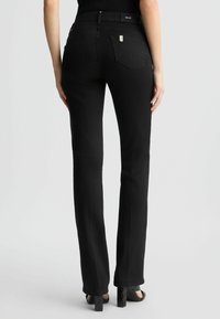 Pantalon noir à jambe droite avec une taille mi-haute, doté d'un logo argenté et de deux poches arrière, fabriqué en tissu lisse et extensible.