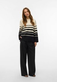 Maglione a righe in crema e navy, con maniche larghe. Abbinato a pantaloni neri larghi. Testura morbida, vestibilità rilassata.