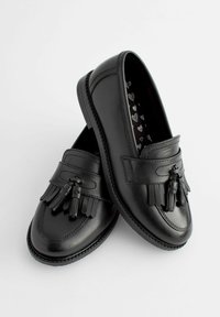 Mocasines de piel negra con textura suave, que presentan borlas decorativas y detalles cosidos. La plantilla tiene un patrón de corazones.