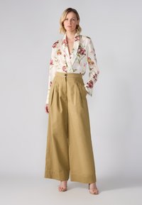 Floral-patterned satin blouse in cream, paired with high-waisted, wide-legged khaki trousers. Features a button and pleated detailing.